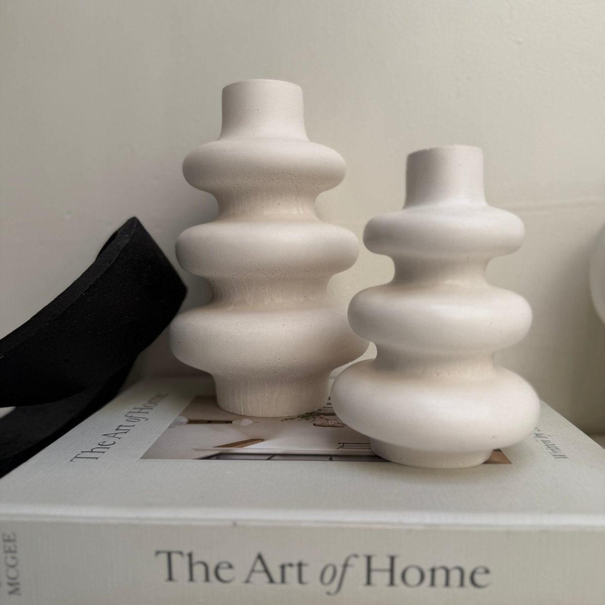 Two white ceramic vases on a book titled 'The Art of Home'.