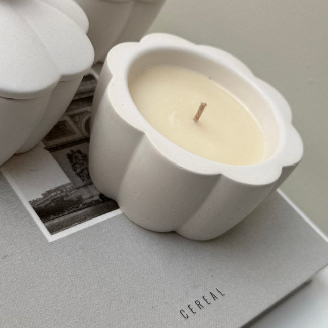 White ceramic flower shaped candle on a gray surface with a black and white photo underneath.