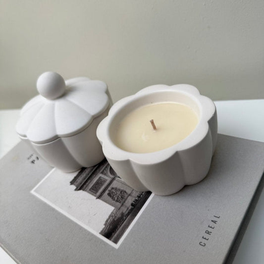 White ceramic container candle with a lid and a white candle inside on a gray surface.