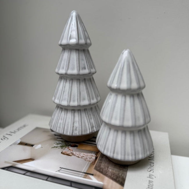 Two ceramic Christmas tree figurines on a magazine with a plain background
