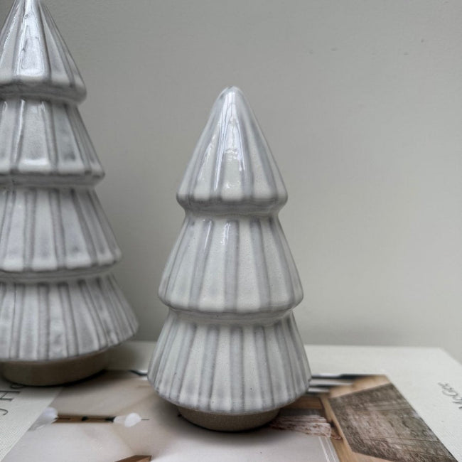 Two gray ceramic Christmas tree decorations on a white surface with a neutral background.