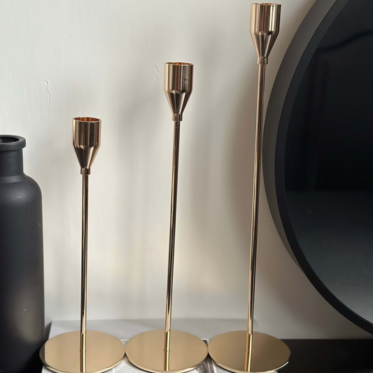 A set of three gold contemporary taper candle stands of varying heights, displayed against a neutral background.