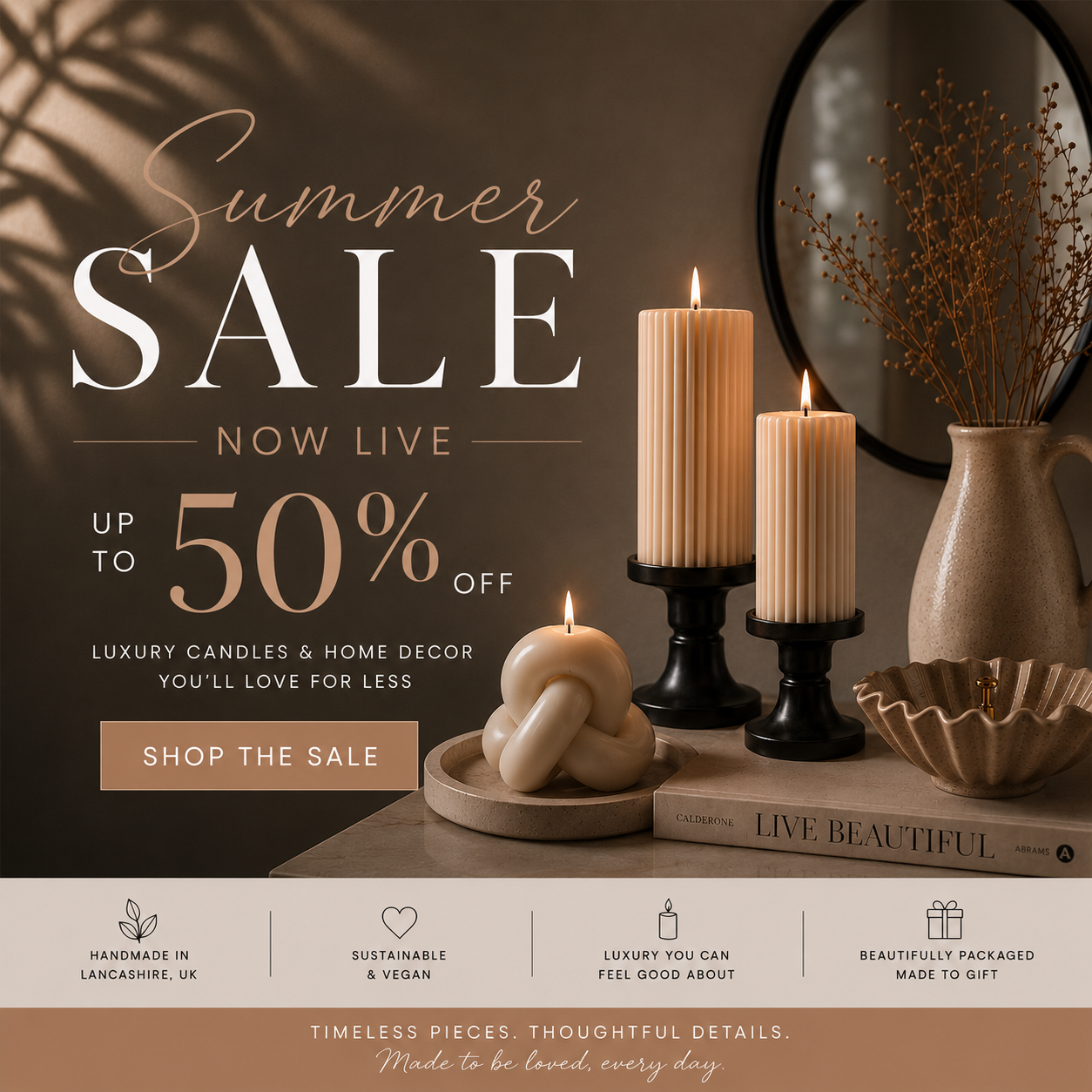 Promotional banner for a summer sale featuring luxury candles and home decor. The scene shows three lit cream-colored pillar candles in black holders, a knotted candle on a wooden tray, and dried floral arrangements in a ceramic vase, set against a warm, shadowed background with a mirror and a book.