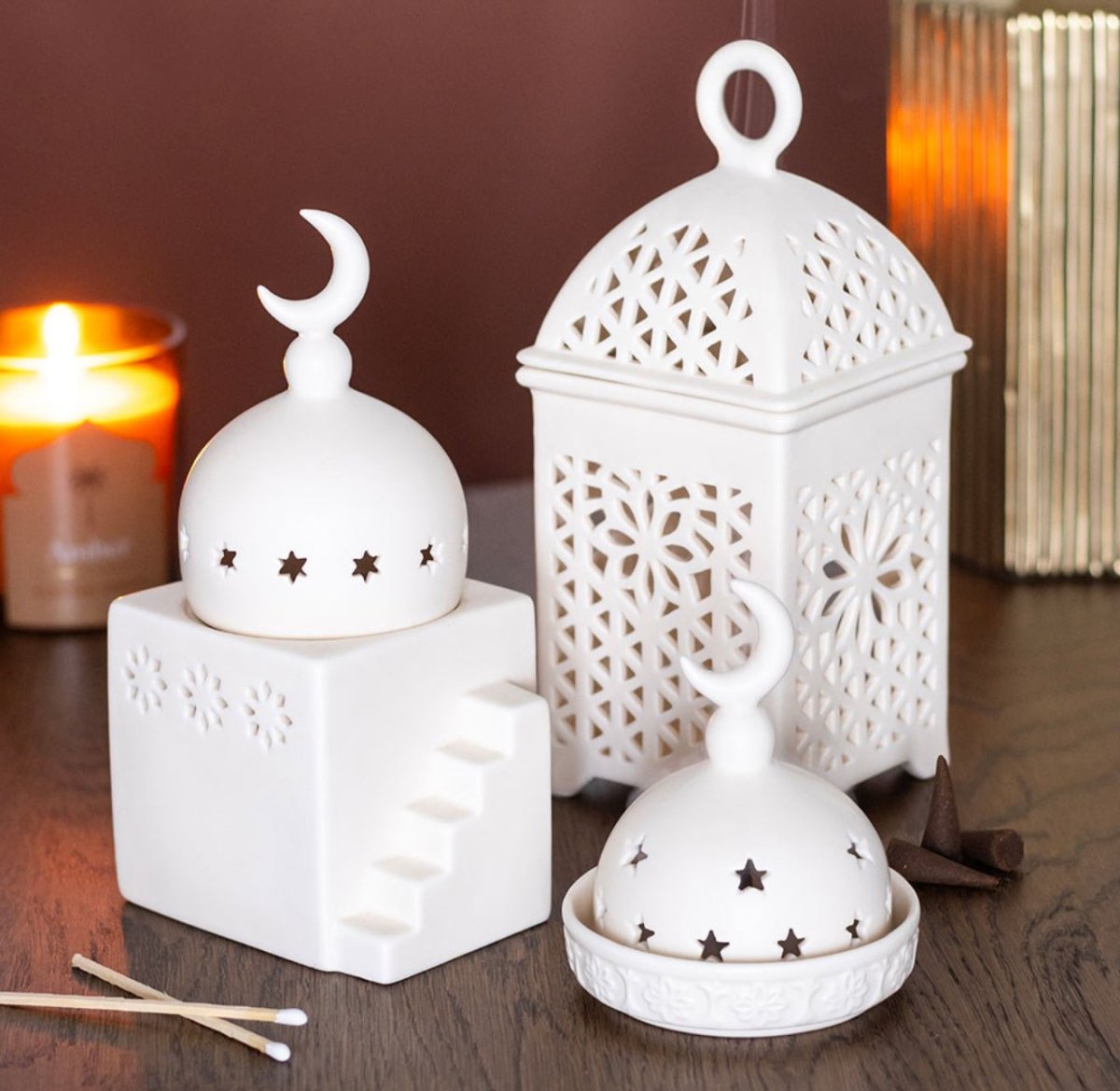 Set of white ceramic lanterns and decorative items on a wooden surface with a candle in the background.
