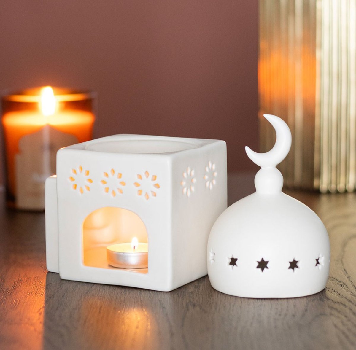 Two white ceramic lanterns on a wooden surface with a blurred candle in the background.