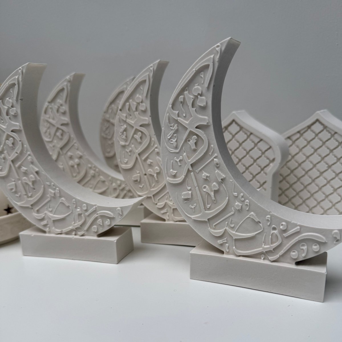Decorative white crescent moon stone art with intricate Arabic patterns on a plain background