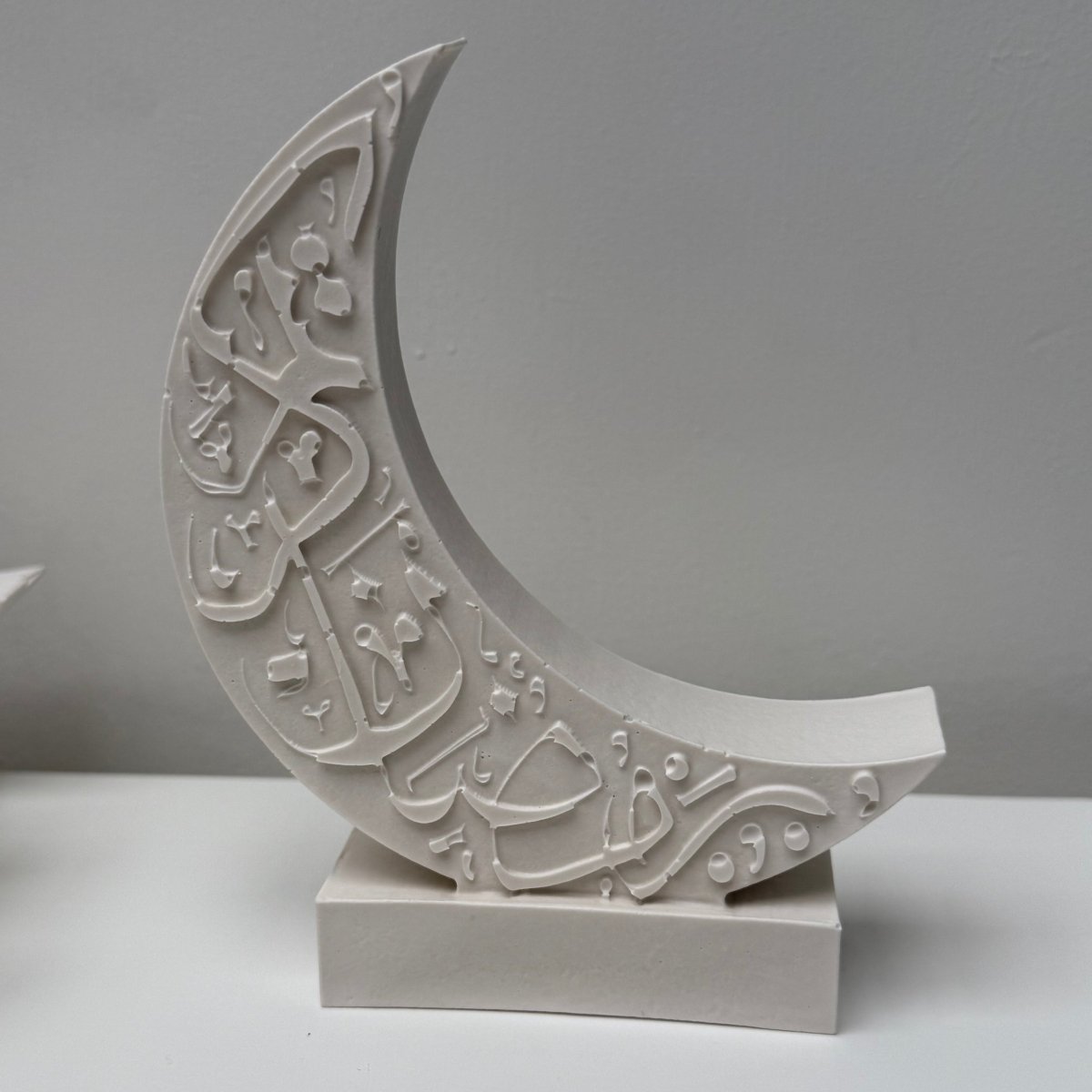 Decorative white crescent moon stone sculptural decor with intricate Arabic patterns on a plain background