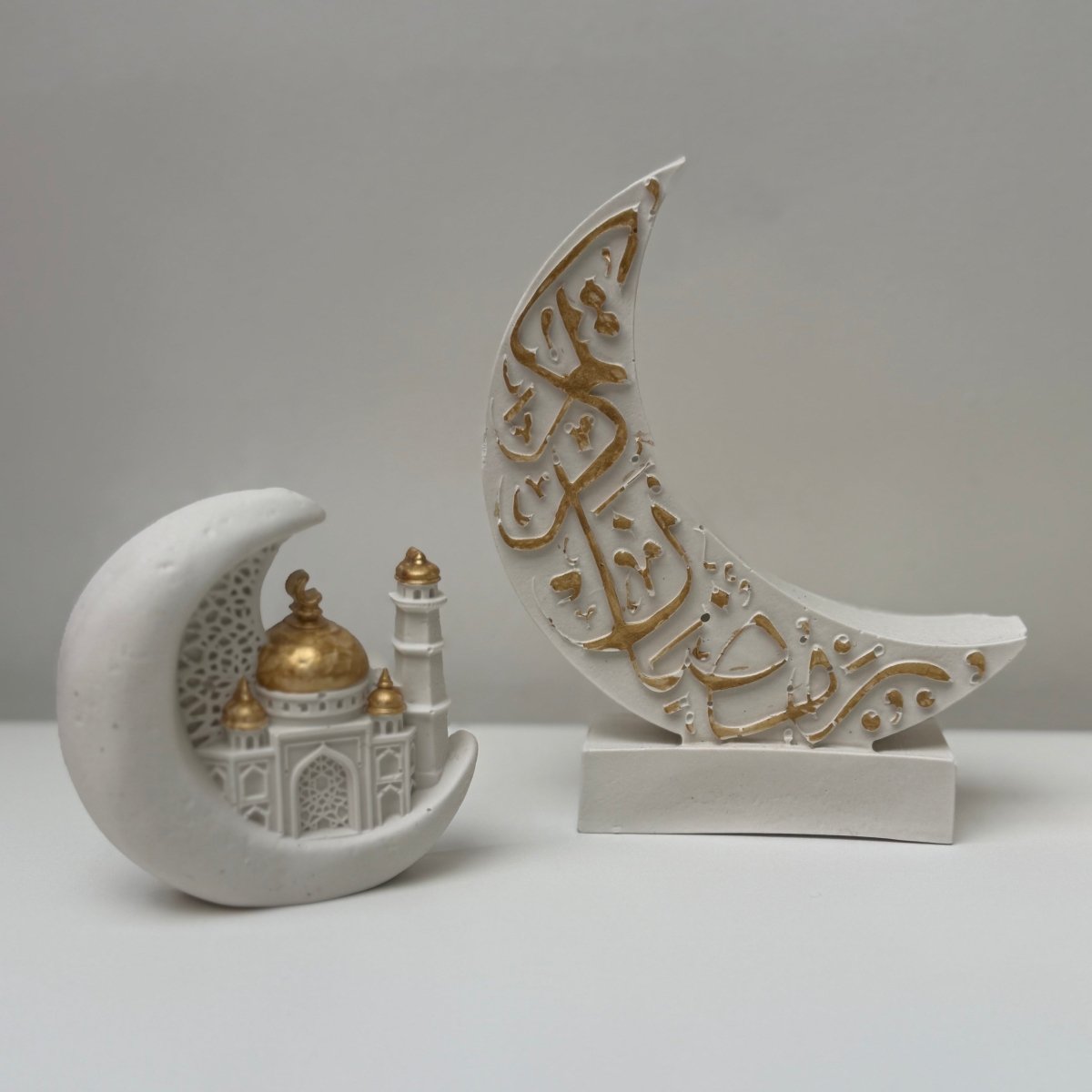 Decorative crescent moon with intricate arabic designs and a small building model on a plain background