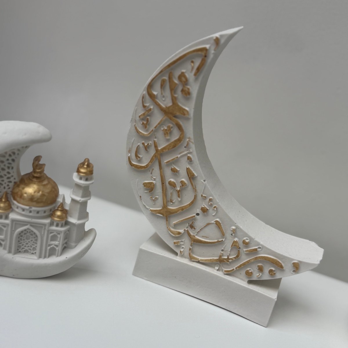Decorative crescent moon with Arabic text and a miniature model of a mosque on a white background