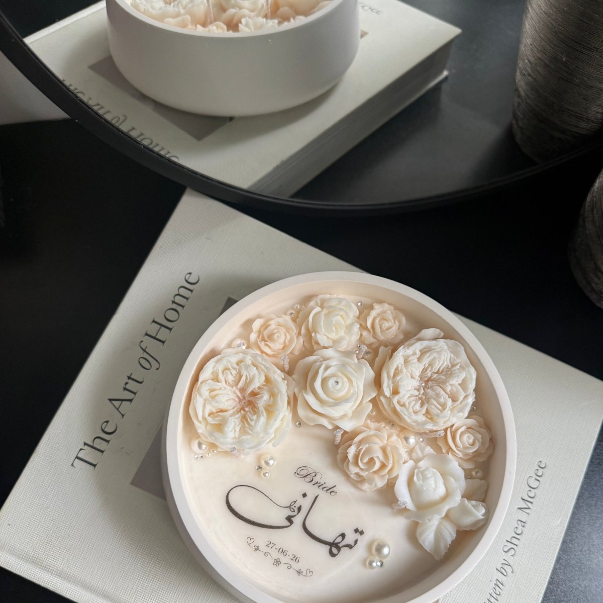 Decorative container Candle with floral design on a book titled 'The Art of Home'.