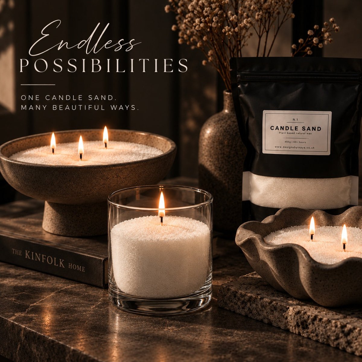 A styled product scene showing a lit candle sand in a clear glass vessel in the foreground, with additional candle sand in sculptural bowls and a black resealable pouch labeled Candle Sand. Decorative dried stems, a vase, a book, and warm ambient lighting create a rich interior setting.