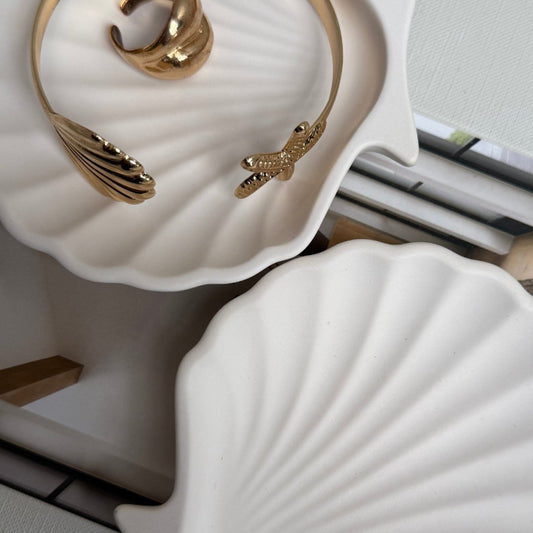 Gold braclet and ring on a white shell-shaped stand.