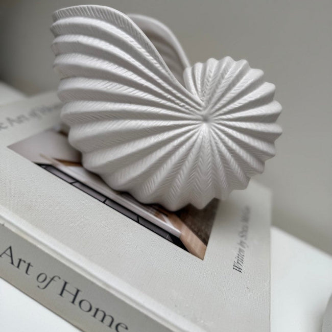 White decorative object resembling a shell on top of a book titled 'Art of Home'.