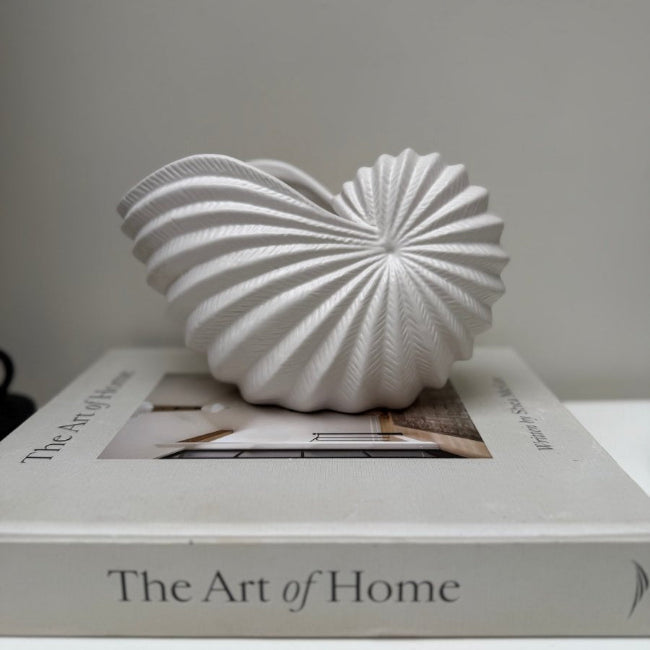 White decorative shell on a book titled 'The Art of Home' with a plain background