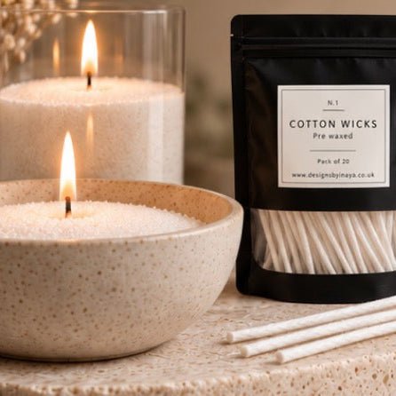 A pack of N.1 Cotton Wicks pre-waxed cotton wicks in a black resealable pouch, shown beside two lit candles in bowls on a textured stone surface.