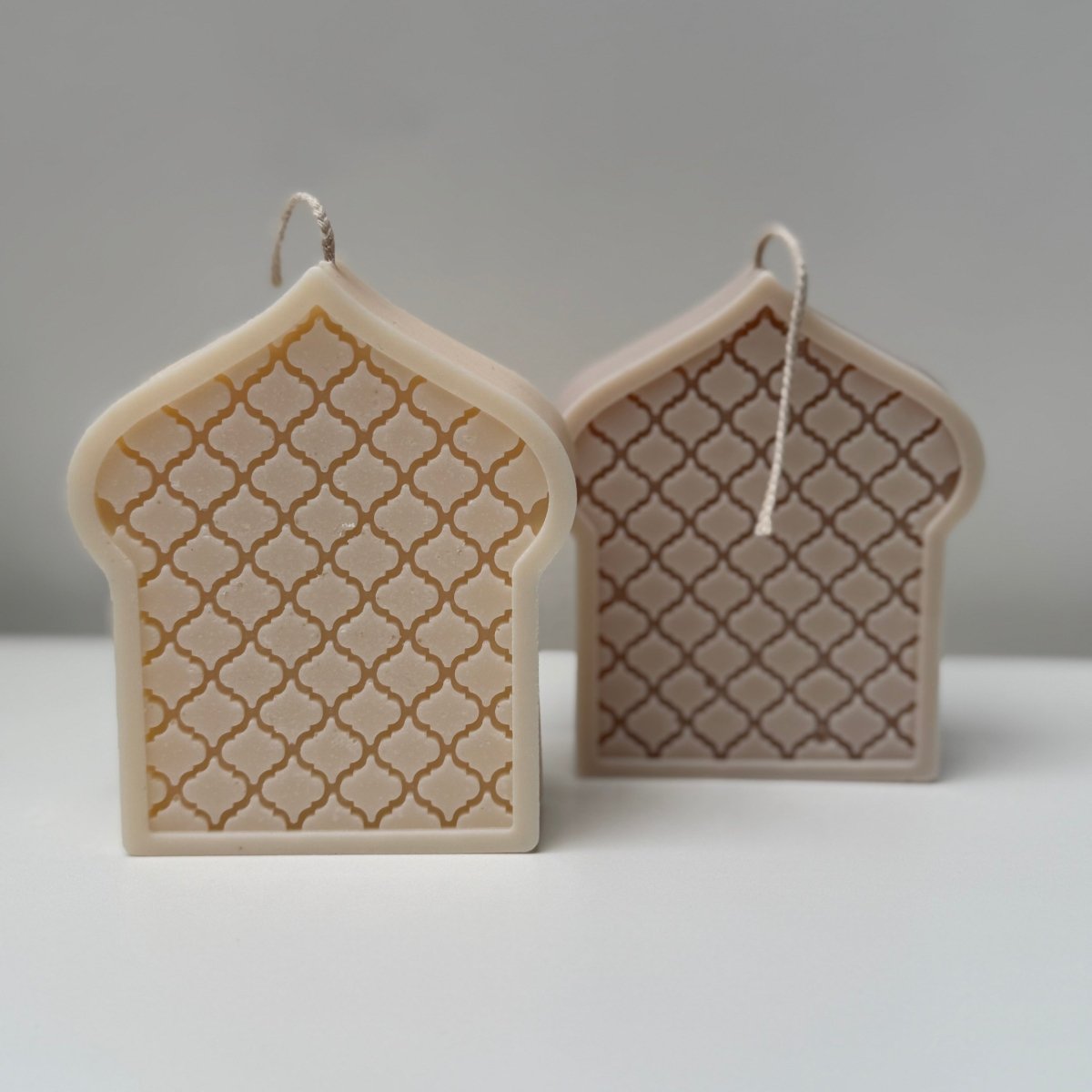 two decorative mosque dome-shaped candles with lattice design on a gray background