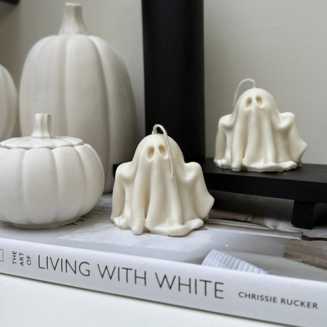 White ghost candles on a book with pumpkins and a black bottle in the background