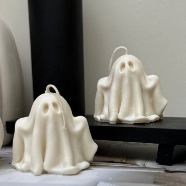 Two ghost-shaped candles on a stack of books with a pumpkin in the background