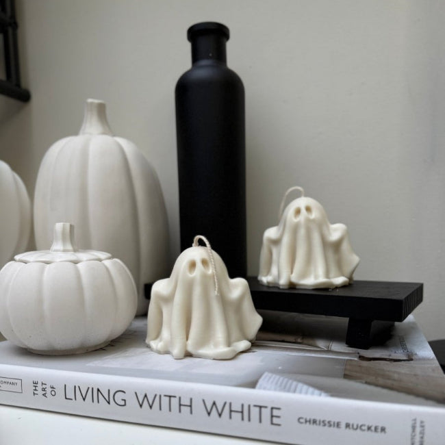 White ghost candles on a book with pumpkins and a black bottle in the background