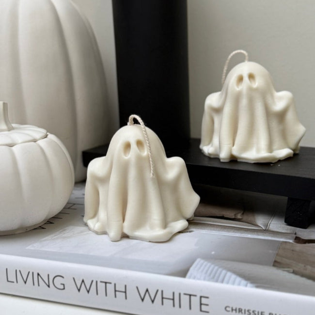 White ghost-shaped candles on a book with pumpkins in the background