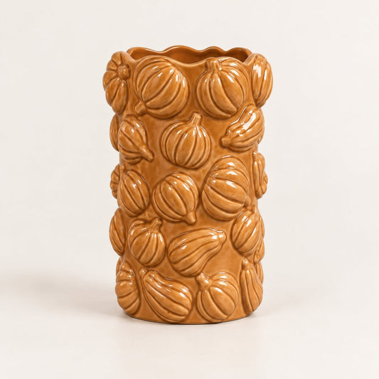 A glazed ceramic vase featuring a raised relief pattern of small pumpkins, in a warm terracotta orange-brown colour, set against a plain light background.