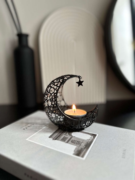 Contemporary black metal moon & Star shaped tea light candle holder with intricate details, lit tea light placed on top.