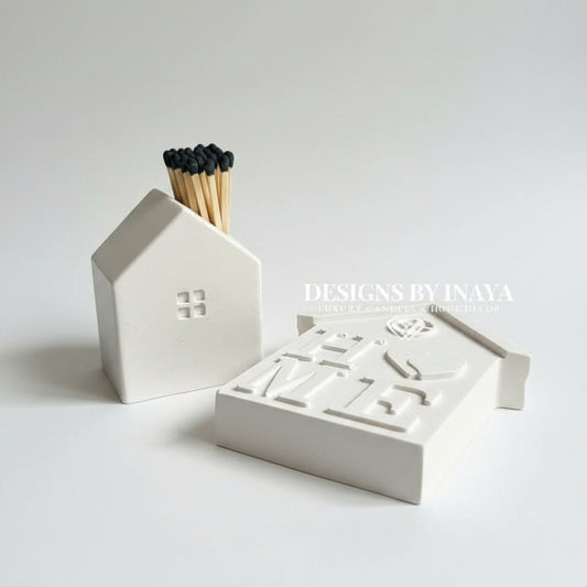 White house-shaped ceramic match holder set on a light background, with matches inserted into the front holder and embossed lettering on the HOME ornament.