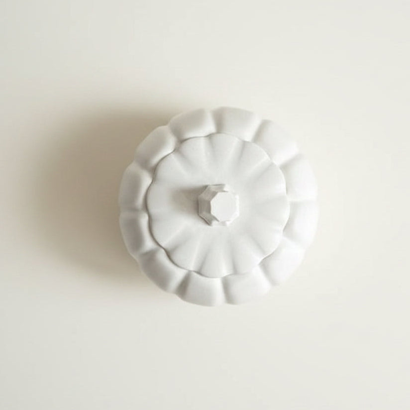 A white jesmonite stone decorative lidded container or vase with a scalloped, pumpkin-like rim and a small hexagonal knob on top, shown against a plain off-white background.