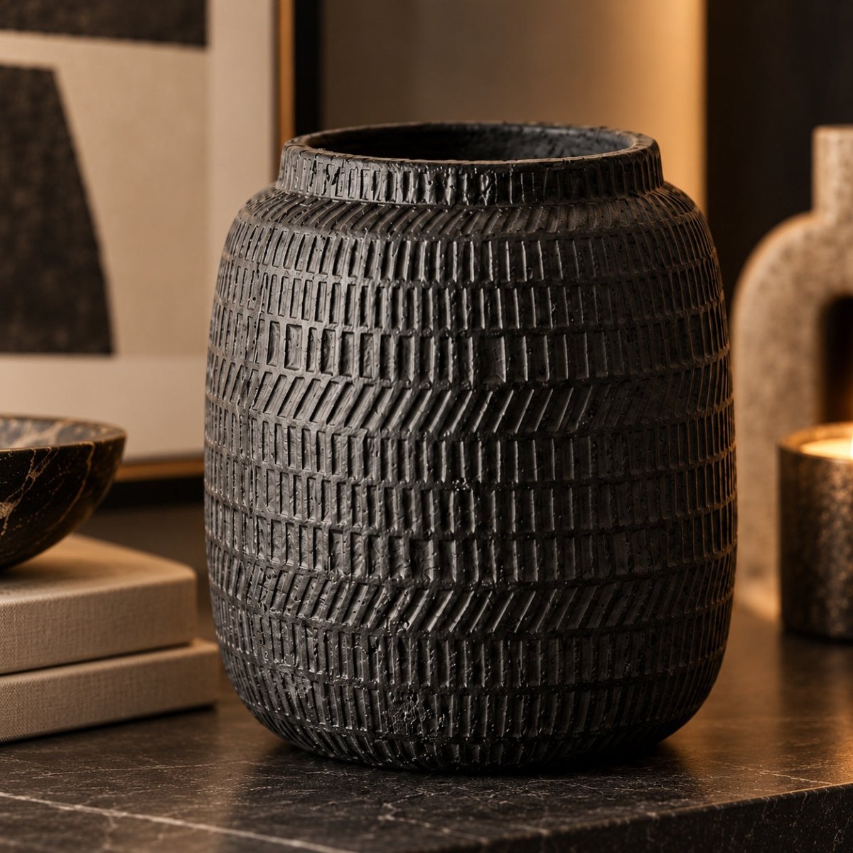 A dark textured ceramic vase with a basketweave pattern, displayed on a dark marble surface in a warm, modern interior setting.