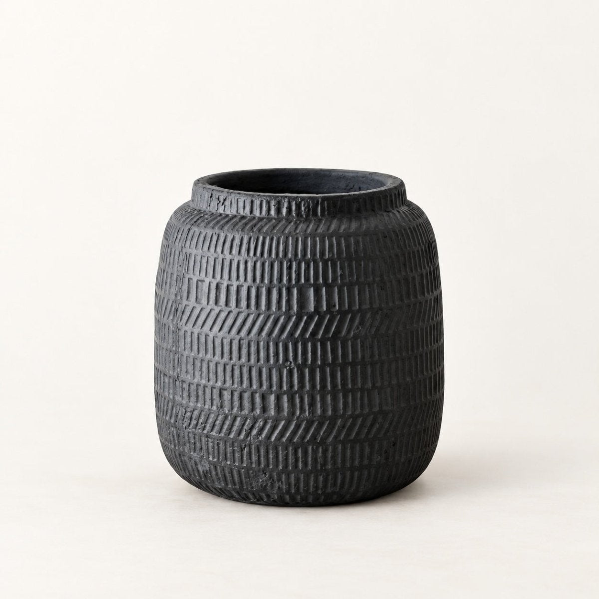 A dark charcoal black textured ceramic pot with a ribbed basketweave pattern, photographed against a clean off-white background.