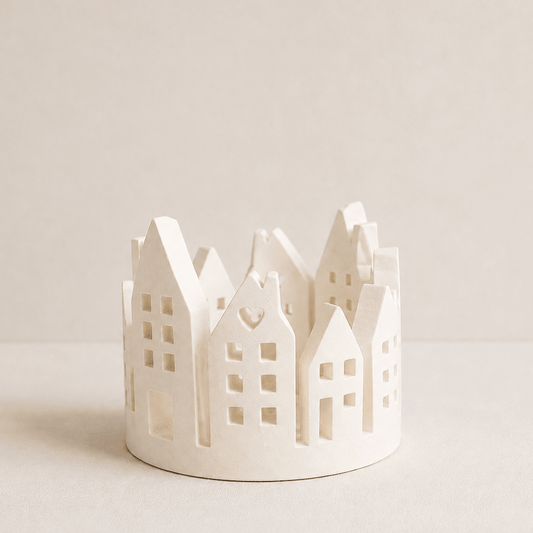 A small white Jesmonite candle holder shaped like a row of traditional house rooftops, photographed on a clean, solid light beige background. Designs by Inaya