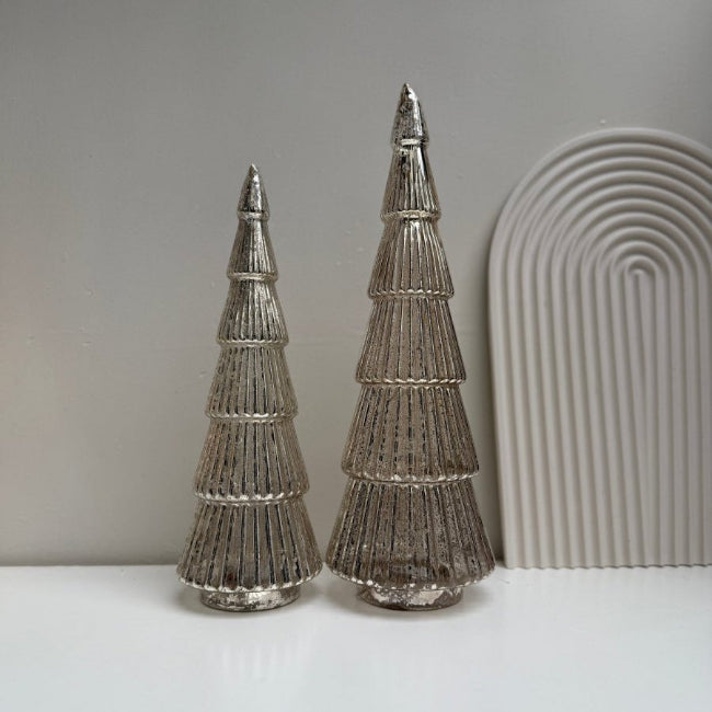 Two metallic tree-shaped decorations on a white surface with a neutral background