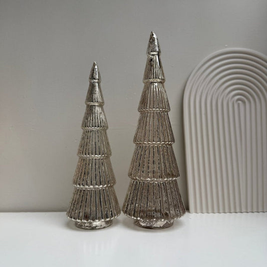 Two metallic tree-shaped decorations on a white surface with a neutral background