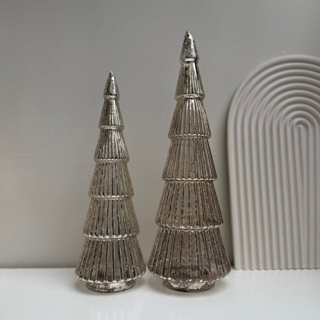 Two metallic decorative trees on a white surface with a gray background