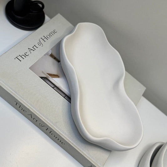 White ceramic dish on top of a book titled 'The Art of Home' with a black candle holder.