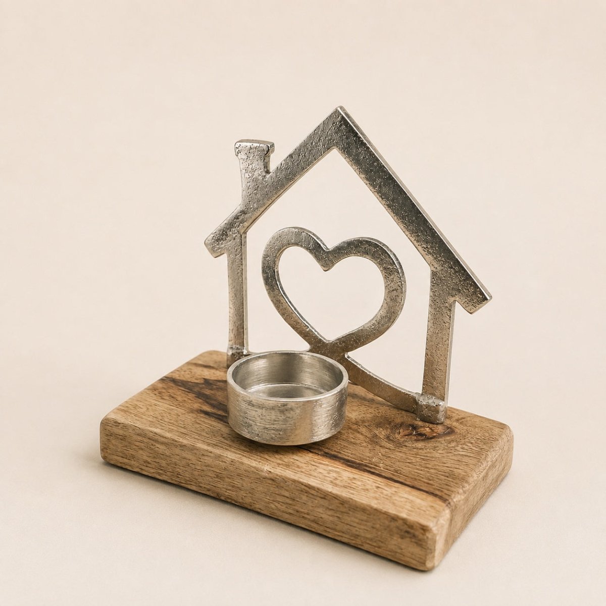 A rustic metal house-shaped candle holder with a heart cutout and a small round metal tea light cup, set on a rectangular wooden base against a warm beige background.