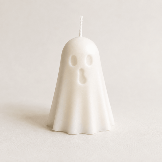 A ghost-shaped candle in an off-white color with a simple molded face and a single wick, for Halloween styling, set against a neutral light beige background. 