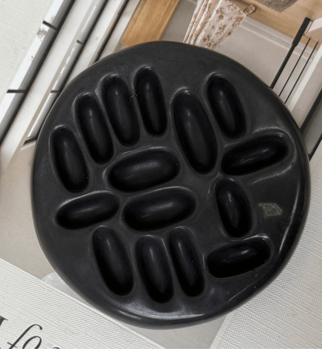 Black ceramic ring holder with oval cavities on a light wooden surface.