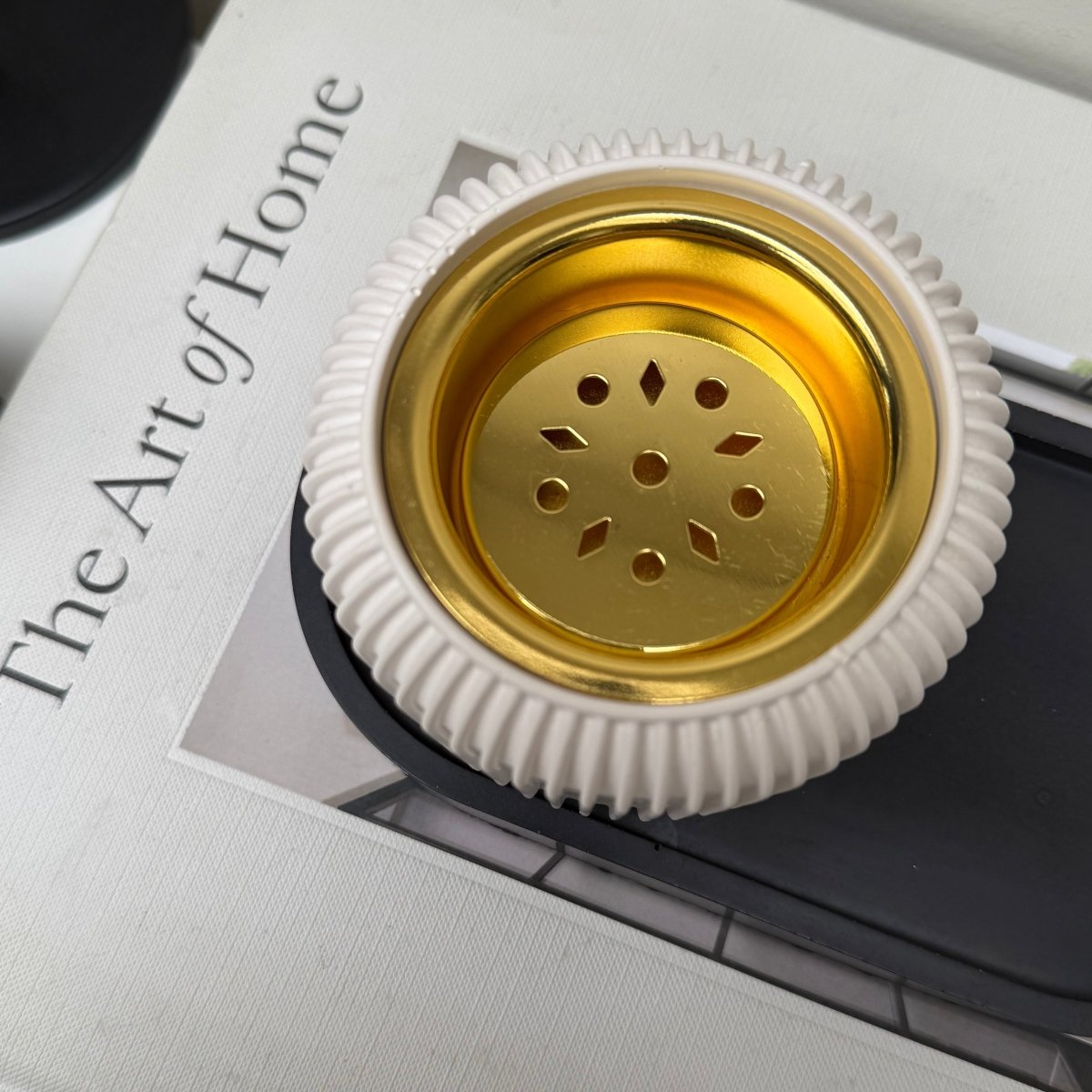 Modern stone bakhoor incense burner featuring a gold-tone removable plate set on a decorative book.