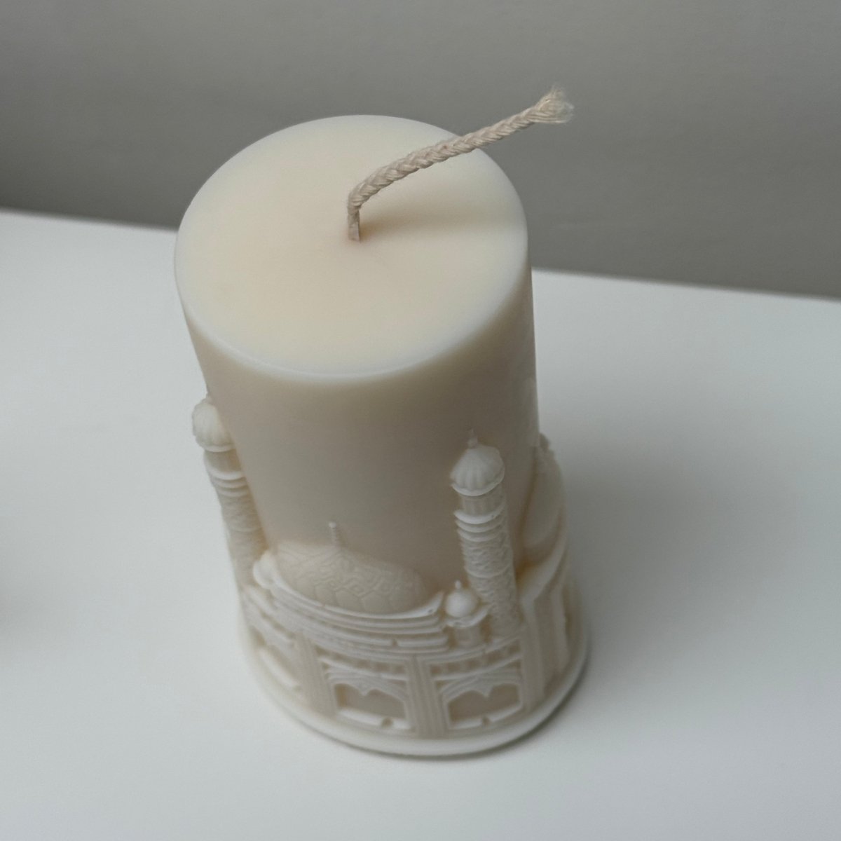 White candle with decorative base on a white surface