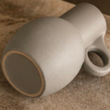 A ceramic vase with a rounded, bulbous body and a loop handle, shown resting on a textured stone surface.