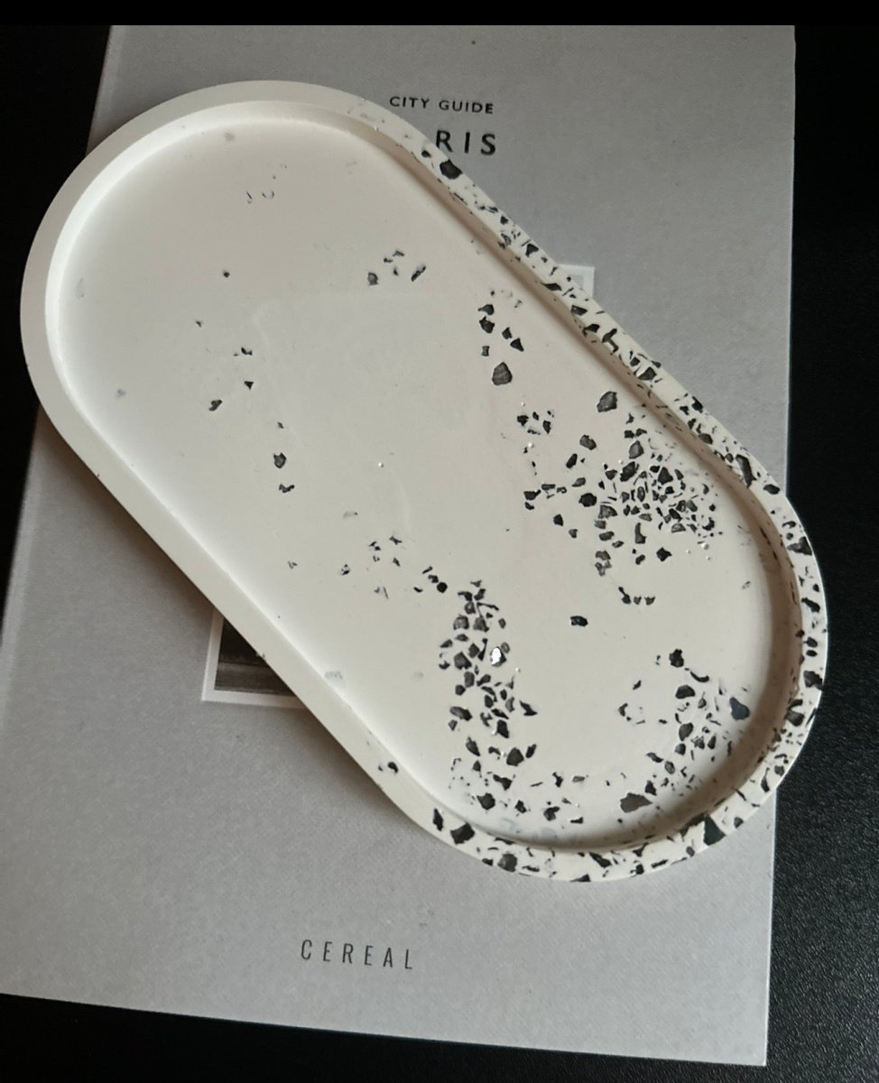 An oval white tray with a black speckled terrazzo pattern around the rim, resting on a light gray cereal box.