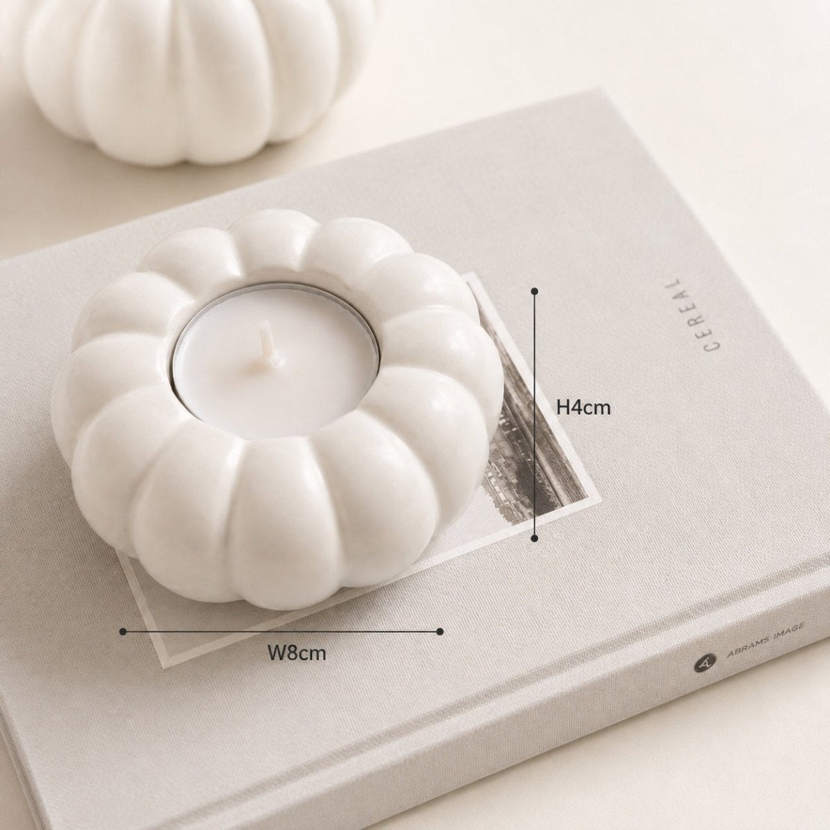 A white handmade Jesmonite tealight candle holder with a ribbed pumpkin-like shape, shown on top of a light gray book with overlaid dimension markers indicating 8 cm width and 4 cm height.