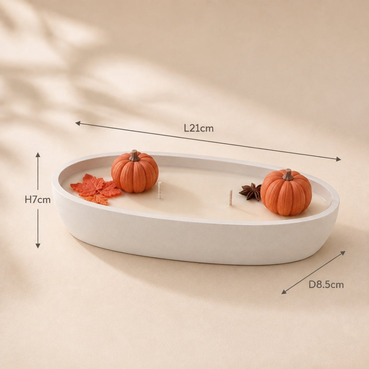 An oval white ceramic candle holder with two small orange pumpkins, a red leaf, and a star anise inside, shown with dimension lines indicating a length of 21cm, height of 7cm, and depth of 8.5cm on a beige background.