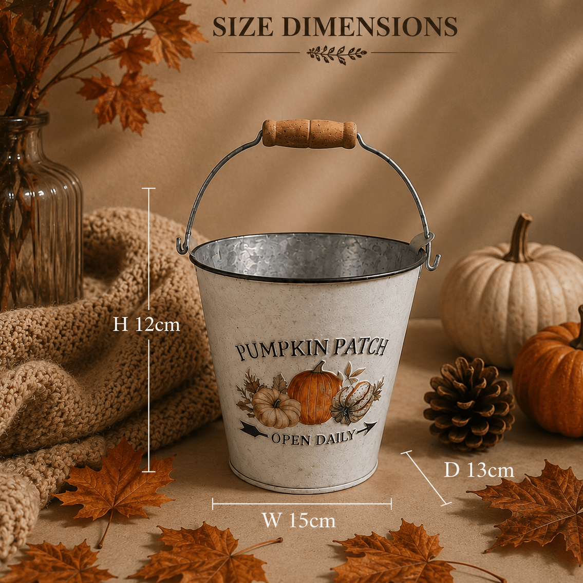 A decorative Zinc metal planter with a wooden handle and printed autumn text reading 'PUMPKIN PATCH' and 'OPEN DAILY,' shown with overlaid size dimensions (H 12cm, W 15cm, D 13cm) on a styled autumn background with pumpkins, leaves, and a knitted textile.