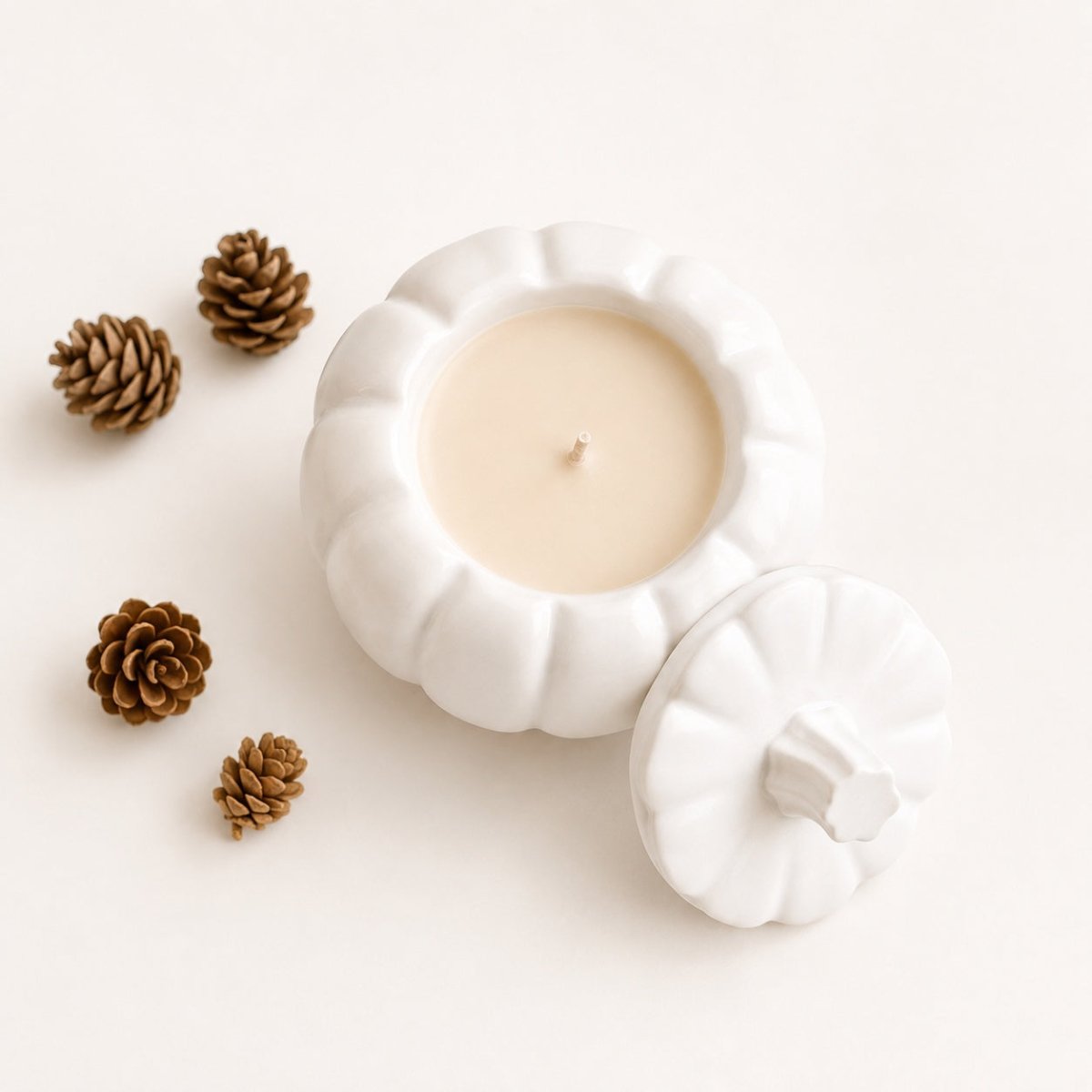 A white Jesmonite pumpkin-shaped candle with its lid placed beside it on a clean white background, styled with four small pinecones.