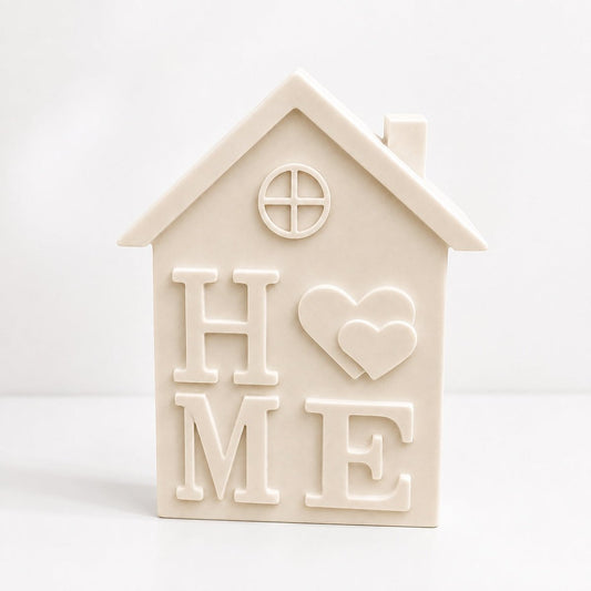 A off white handmade stone house-shaped decorative piece with the word 'HOME' and two hearts embossed on the front, set against a plain white background.