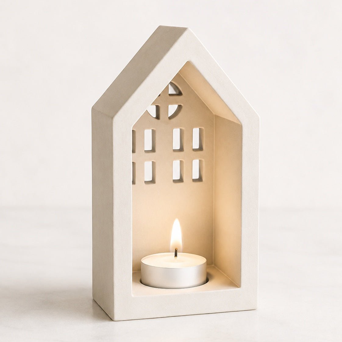 A house-shaped stone candle holder with a lit tea light candle inside, set against a clean, light off-white background.