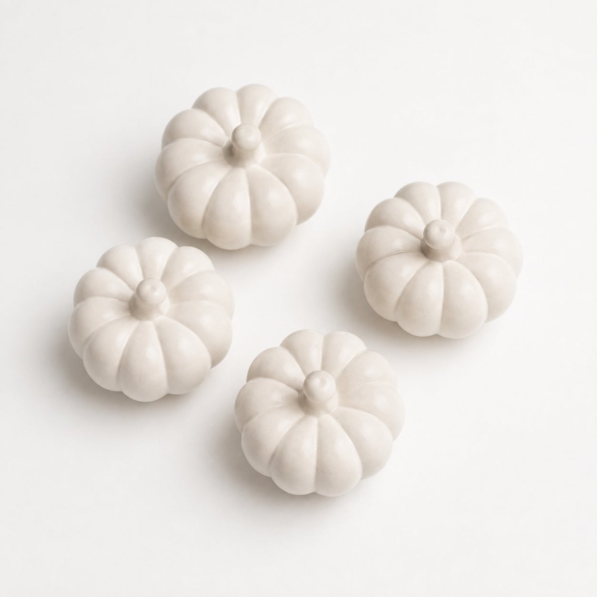 Four small decorative pumpkin-shaped ornaments in a matte off-white finish, arranged on a clean white background.