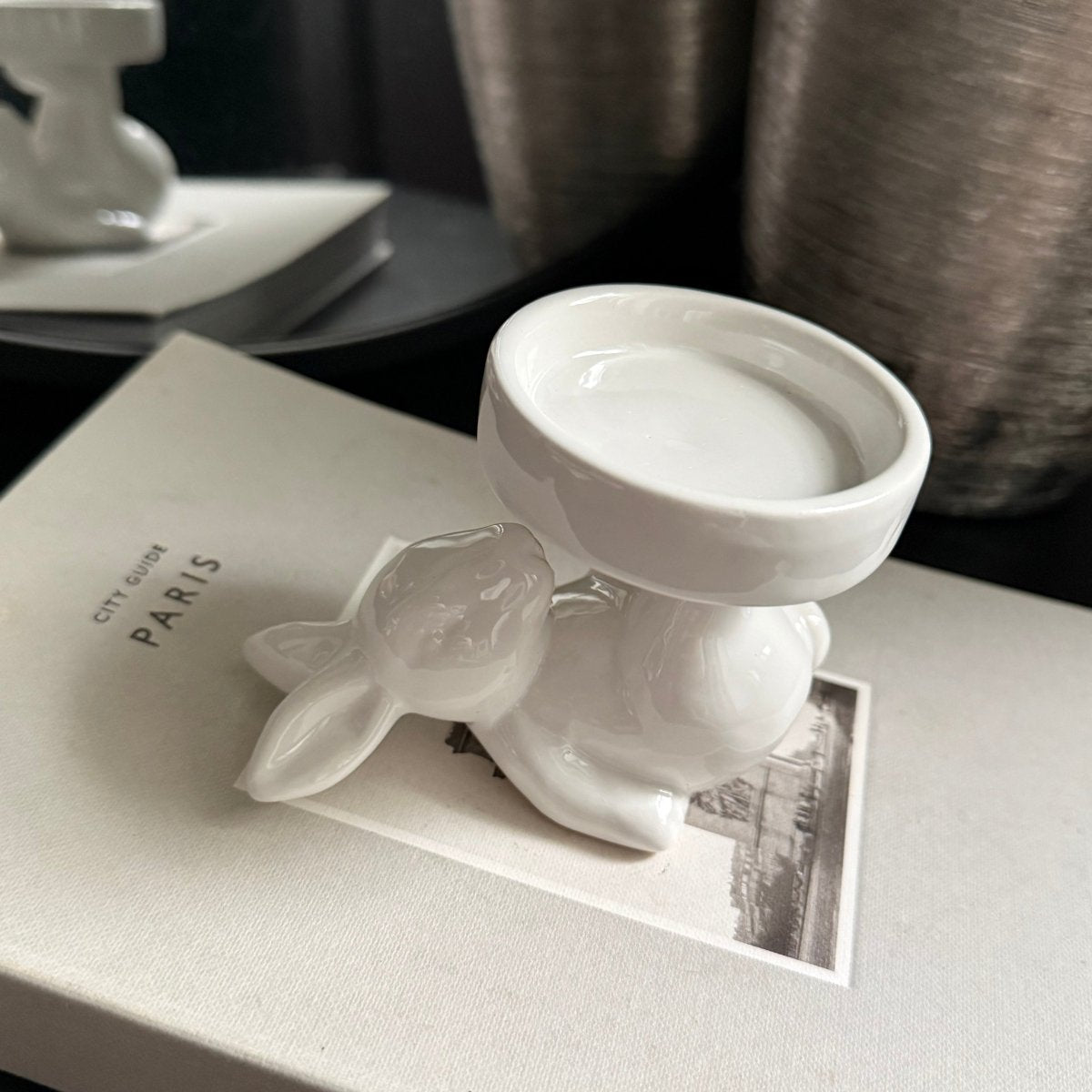 white ceramic rabbit candle holder - White ceramic rabbit figurine on a gray surface with 'PARIS' branding.
